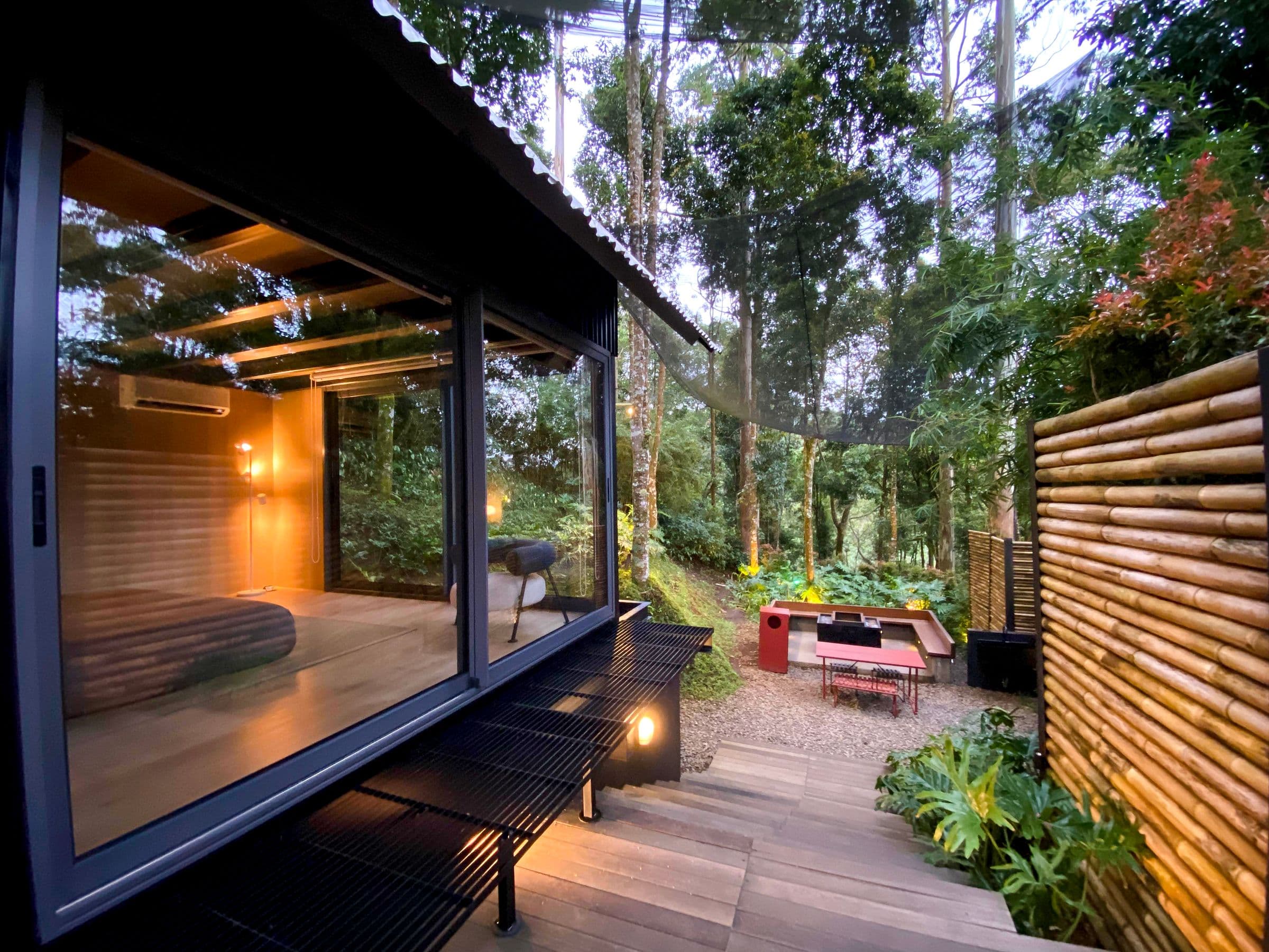 Modern black timber cabin opening onto a mature woodland garden